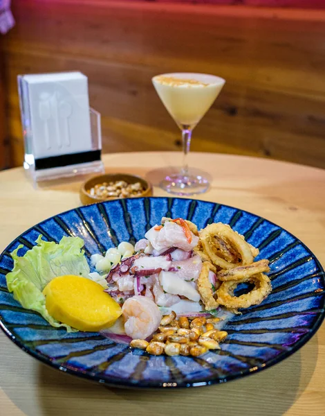 Pisco ve kızarmış mısırla birlikte mavi bir tabakta servis edilen Peru ceviche 'si.