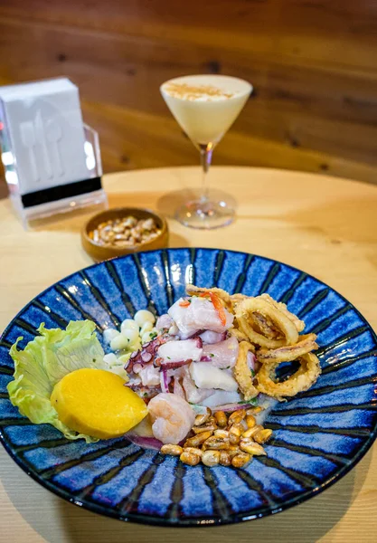 Pisco ve kızarmış mısırla birlikte mavi bir tabakta servis edilen Peru ceviche 'si.