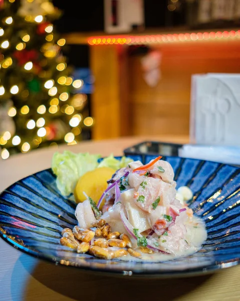 Peru ceviche 'si mavi bir tabakta sunuluyor, arka planda Noel ışıkları var.