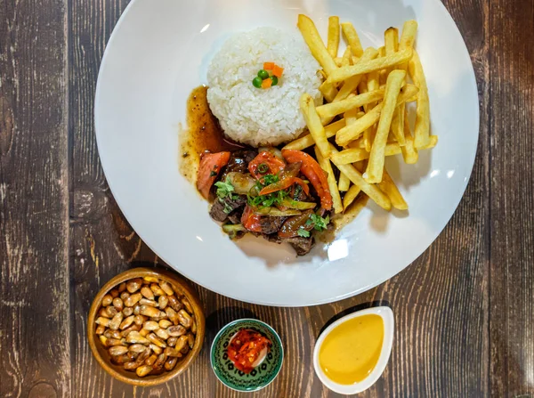 Lomo saltado, beyaz pirinç ve patates kızartması, ahşap masa üzerinde servis ediliyor.