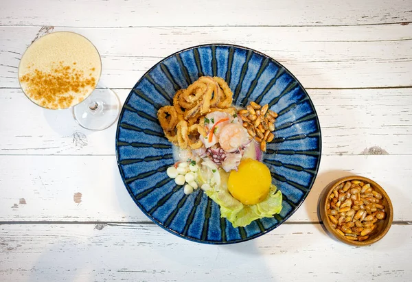 Peru ceviche, yanında Pisco ve beyaz ahşap arka planda kızarmış mısırla mavi bir tabakta servis edildi.