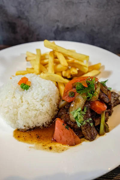 Lomo saltado, beyaz pirinç ve patates kızartması, ahşap masada servis edilir.