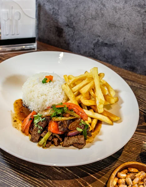 Lomo saltado, beyaz pirinç ve patates kızartması, ahşap masa üzerinde servis ediliyor.