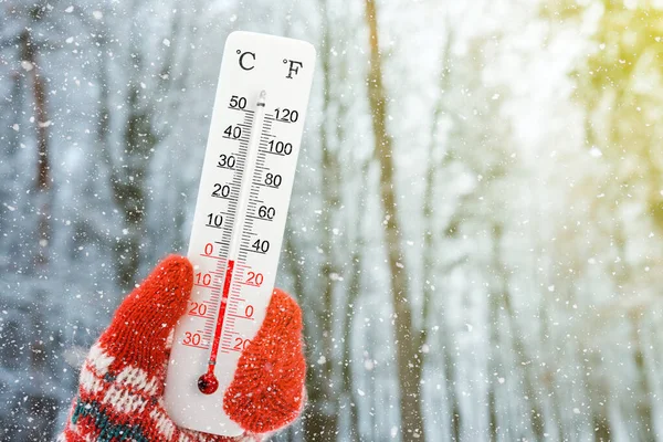 White celsius and fahrenheit scale thermometer in hand. Ambient temperature zero degrees celsius