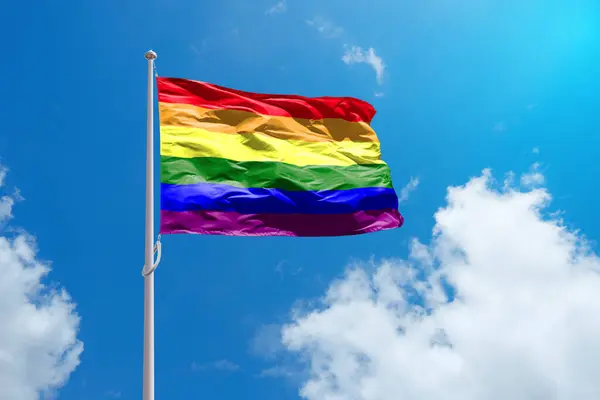 stock image Waving LGBT rainbow flag above blue sky