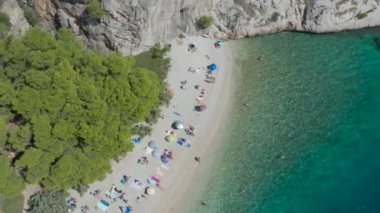 Dağlar ve ormanlar arasında güzel bir sahil. Hırvatistan. Makarska Riviera. Temiz mavi su ve çam aromalı Adriyatik Denizi gölü. İnsansız hava aracı videosu. Tatilde. Bir sürü insan. Nugal Plajı