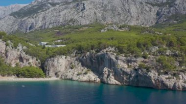 Dağlar ve ormanlar arasında güzel bir sahil. Hırvatistan. Makarska Riviera. Temiz mavi su ve çam aromalı Adriyatik Denizi gölü. İnsansız hava aracı videosu. Tatilde. Bir sürü insan. Nugal Plajı