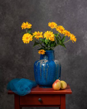 Kırmızı, ahşap bir masada huzur ve konfor. İki sarı armut, bir buket sarı sonbahar çiçeği büyük mavi kil bir vazoda. Koyu gri arka plan. Kavunkolisi. Durgun hayat.