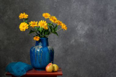 Kırmızı, ahşap bir masada huzur ve konfor. İki sarı armut, bir buket sarı sonbahar çiçeği büyük mavi kil bir vazoda. Koyu gri arka plan. Kavunkolisi. Durgun hayat.