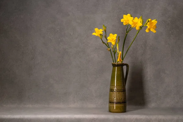 一些黄色的百合花在一个绿色的粘土花瓶与一个柄在灰色的背景 平静的生活 简约主义美存在于简单之中 恭喜你假期 — 图库照片