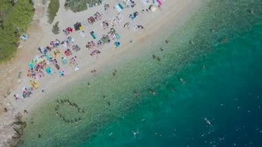 Hırvatistan 'ın Makarska kenti yakınlarındaki mavi göldeki gözlerden uzak çıplaklar plajında. Tatilciler sıcak Adriyatik Denizi 'nde eğleniyorlar. Yaz tatili, güneş banyosu, temiz hava. İHA görüntüsü. Nugal Plajı. Rahatla.