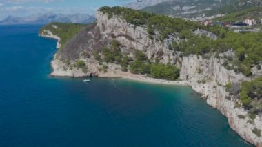 İnsansız hava aracı Nugal sahilinde uçuyor. Dağ denizin üzerinde asılı. Çam ağaçları, kayalar, mavi deniz suyu. Tekne bedava. Uzakta yanmış bir orman. Birçok tatilci vahşi sahilde.