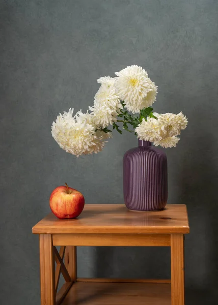 很多白色的花 在木制桌子上的紫色花瓶里放着一束白色的衬托 旁边有一个红苹果 灰色背景 维生素 生活的快乐 小心点注意了 — 图库照片