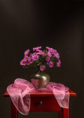 Kırmızı ahşap bir masada pembe astar buketi. Koyu gri arka plan. Yakınlarda pembe bir eşarp var. Kart. Duvar için bir tablo. Durgun hayat. Dilekler. Kutlarım. Bir buket çiçek..