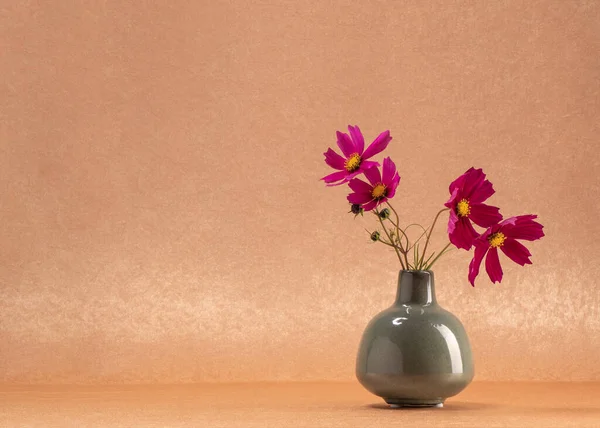 Four dark pink flowers in a gray vase on an orange background. Still life for postcards, congratulations. Freshness, comfort, wishes, tranquility.