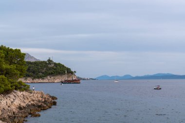 An old wooden boat with many tourists on board. Beautiful rocky coastline. It's evening. Small yachts and boats sail nearby. Croatia.