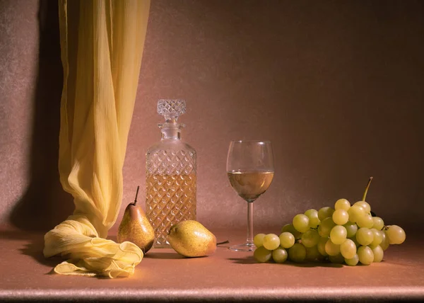 stock image A carafe of white wine, next to a glass of white wine, two pears and a bunch of white grapes on an orange background. With a yellow scarf. Still life.