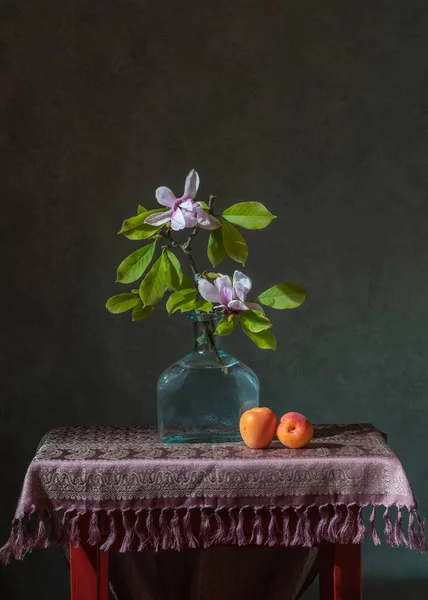 木兰花枝在一个透明的瓶子里 旁边有两个桃子 — 图库照片