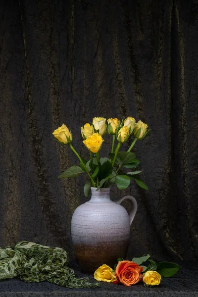 Bouquet of yellow roses in a vase, jug. Dark fabric background. Nearby are three roses. Place for an inscription. flower still life