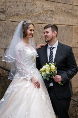 Güzel, genç bir gelin nazikçe damada bakar. Damat onun elini tutuyor. Eski bir kalenin arka planında yürümek, binalar. Aşk ve uyum, genç aile.