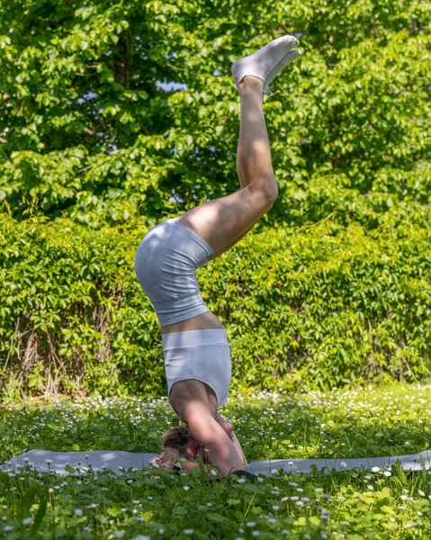 A young, athletic girl is engaged in stretching  in the fresh air. Beauty, sports and health. Active lifestyle. Physical exercise. Headstand