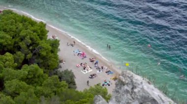 Güzel, vahşi bir plajda, turistler şeffaf, mavi bir denizde banyo yapıyorlar. İnsanlar güneşlenir ve rahatlarlar. Yaz sezonu. Yukarıdan görüntüle. 