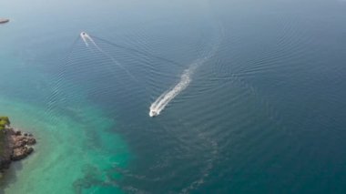 Küçük, motorlu, turistli beyaz bir tekne mavi, şeffaf bir denizde yüzüyor. Sakin deniz. Yukarıdan görüntüle