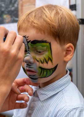 Yüzünde bir desen olan küçük bir çocuğun yüzü. Ressam, bir çocuğun yüzüne yeşil bir ejderha resmi çiziyor.