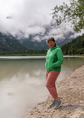 Orta yaşlı bir kadın dünyayı gezer. Dolomitlerin görkemli dağları olan Güney Tyrol 'da gölün yanında duruyor. İtalya.