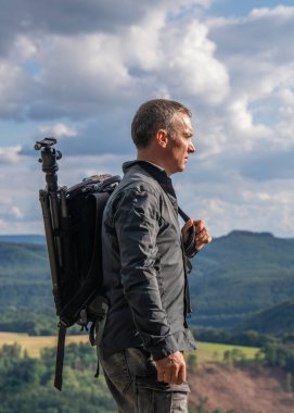 Fotoğrafçı dağların tepesinde duruyor, elinde bir sırt çantası ve kameraya bağlı bir tripodla. Sakson İsviçre, Almanya