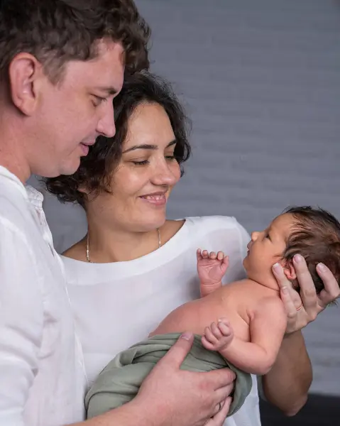 Yeni doğmuş bebeği olan mutlu bir aile. Sevgi dolu bir anne ve baba, küçük oğullarını nazikçe kucaklıyor ve çocuğa şefkatle bakıyor..