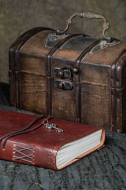 Deri bir çantadaki not defteri eski bir sandığın yanında duruyor. Karanlık arka plan. Hayat, kartpostal.
