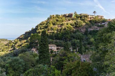İspanya 'nın Mallorca kentindeki Deia adlı küçük bir sahil köyünün çarpıcı manzarası. Yeşil ağaçlarla çevrili tepelerdeki teraslarda geleneksel evler. İspanyol turizm merkezleri.