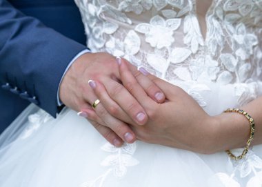 Alyanslı eller. Beyaz bir elbisenin arka planında alyansları olan gelin ve damadın elleri. Damat nazikçe gelinin elini tutar. Düğün..