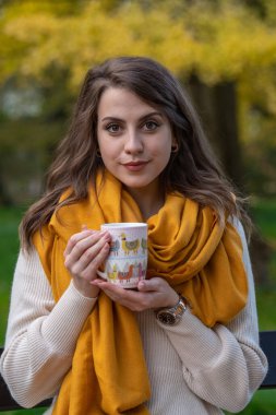 Ellerinde bir fincan ve boynunda sarı bir eşarpla güzel bir genç kızın portresi. Yakın plan.