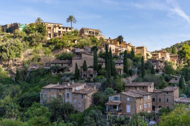 İspanya 'nın Mallorca kentindeki Deia adlı küçük bir sahil köyünün çarpıcı manzarası. Yeşil ağaçlarla çevrili tepelerdeki teraslarda geleneksel evler. İspanyol turizm merkezleri.