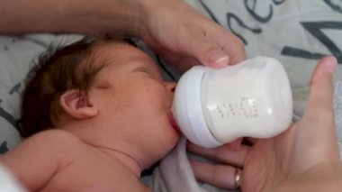 Sevgi dolu bir anne yeni doğan bebeğine bakar. Anne yeni doğan oğlunu biberonla besliyor. Sadece annenin elleri görülebilir. Bebek beşiğinde yatıyor