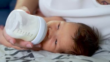 Sevgi dolu bir anne yeni doğan bebeğine bakar. Anne yeni doğan oğlunu biberonla besliyor. Sadece annenin elleri görülebilir. Bebek beşiğinde yatıyor