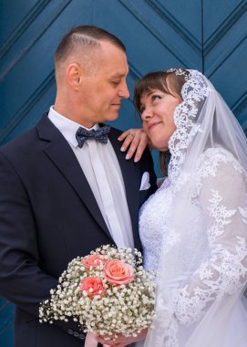 Gelin ve damadın portresi. Gelin nazikçe yüzünü damada bastırdı. Mavi kapıların arkasında. Şefkat, aşk, düğün, duygular