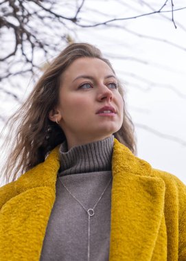 Kendine güveni tam mutlu, sarı ceketli genç bir kadın şehir caddesinde dikilirken yukarı bakıyor, rüya görüyor. 