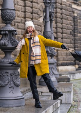 Sarı ceketli zarif bir kadın yeni yerlerden hoşlanıyor. Neşeyle güler, oltayı eliyle tutar. Almanya, Dresden şehrinin turistik yerlerine bakan mutlu gezgin kadın. 
