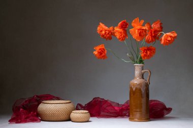 Gelinciklerle hayat. Gri arka planda vazoda kırmızı haşhaş. Yakınlarda iki yuvarlak sepet ve bir kırmızı şal var. Mesaj için yer. Tebrikler, kartpostal.