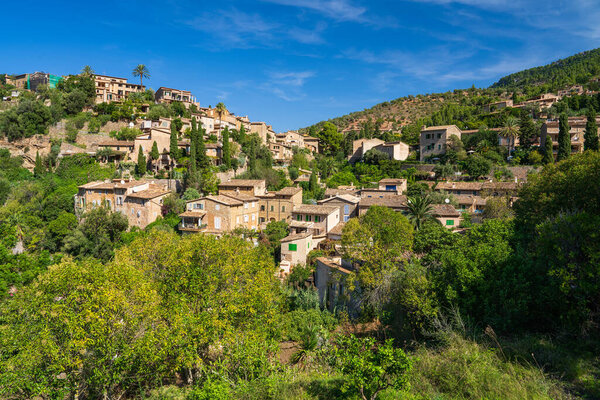 Stunning cityscape of the small coastal village of Deia in Mallorca, Spain. Traditional houses terraced on hills surrounded by green trees. Tourist destinations in Spain. Balearic Islands.