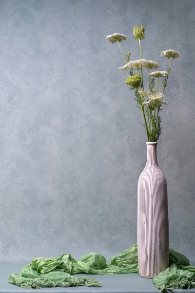 Still life with flowers. White wildflowers in a light tall vase on a light gray background. Congratulations, postcard. Plenty of room for text