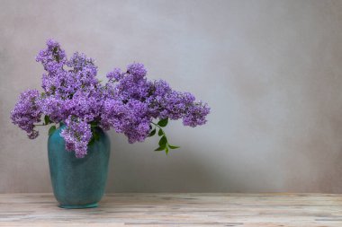 Açık gri arka planda izole edilmiş büyük bir vazoda büyük bir demet leylak. Çiçeklerle dolu sakin bir hayat, metin için bol bol yer. 