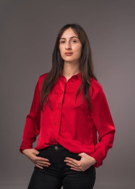Kırmızı gömlekli genç bir kadının portresi, elleri ceplerinde, kameraya doğru bakıyor, yakın plan, gri arka plan
