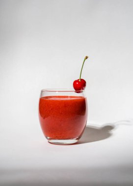 Çilekli bardak, kırmızı smoothie ve beyaz arka planda. Bardakta kiraz var. Yaz içeceği. Vitaminler, diyet, düzgün beslenme, veganlık. 