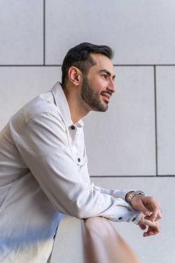 Yakışıklı bir gencin portresi. Sakallı, gülümseyen Asyalı bir adam duvarın yanında duruyor ve düşünceli bir şekilde uzaklığa bakıyor.