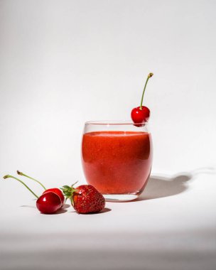 Çilekli bardak, kırmızı smoothie ve beyaz arka planda. Bardakta kiraz var. Yaz içeceği. Vitaminler, diyet, düzgün beslenme, vegan 