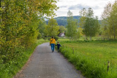 Mutlu bir çocuk kırsal bir yolda el ele yürürken annesinin elini tutar. Küçük bir çocuk elinde bir sopa tutuyor. Ebeveynlik: doğanın tadını çıkaran anne ve oğul